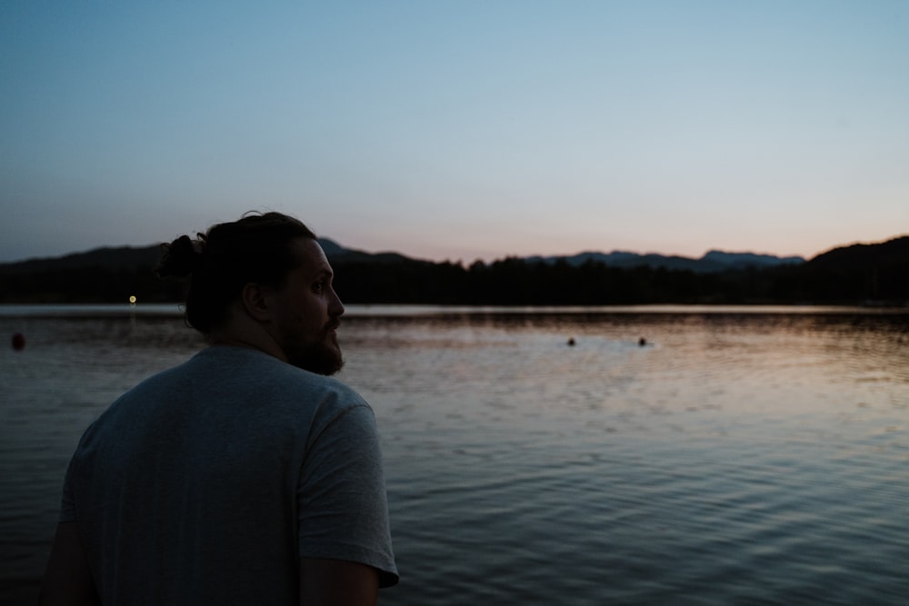 man in white t-shirt standing near lake during daytime