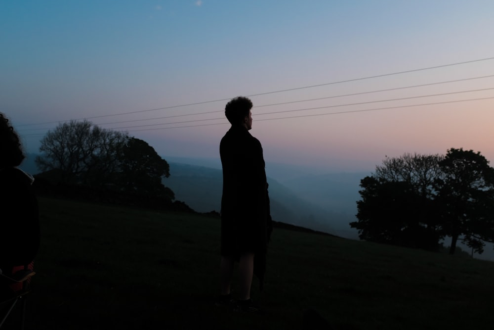 silhouette of woman standing on green grass field during daytime