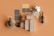 A collection of skincare products displayed on a tan background. The set includes various bottles and boxes featuring dark gray and beige colors with gold accents. A large seashell is placed among the products, adding an organic touch to the arrangement. The items are arranged neatly, highlighting their elegant design and branding.