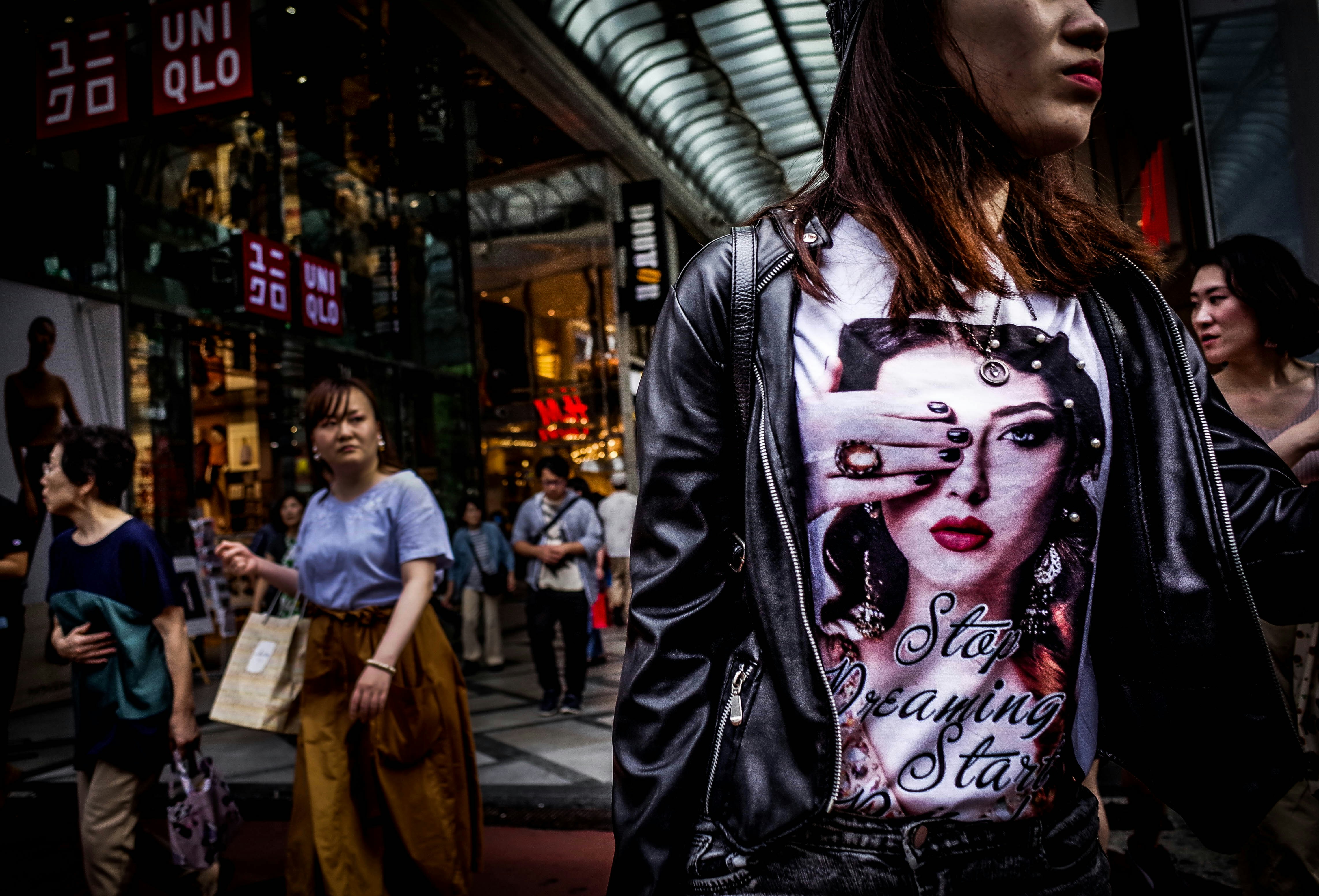 Young woman in oversized graphic jacket and wide leg trousers walking on urban street in natural daylight