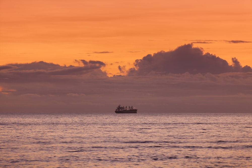 silhouette of ship on sea under blue sky and white clouds during daytime