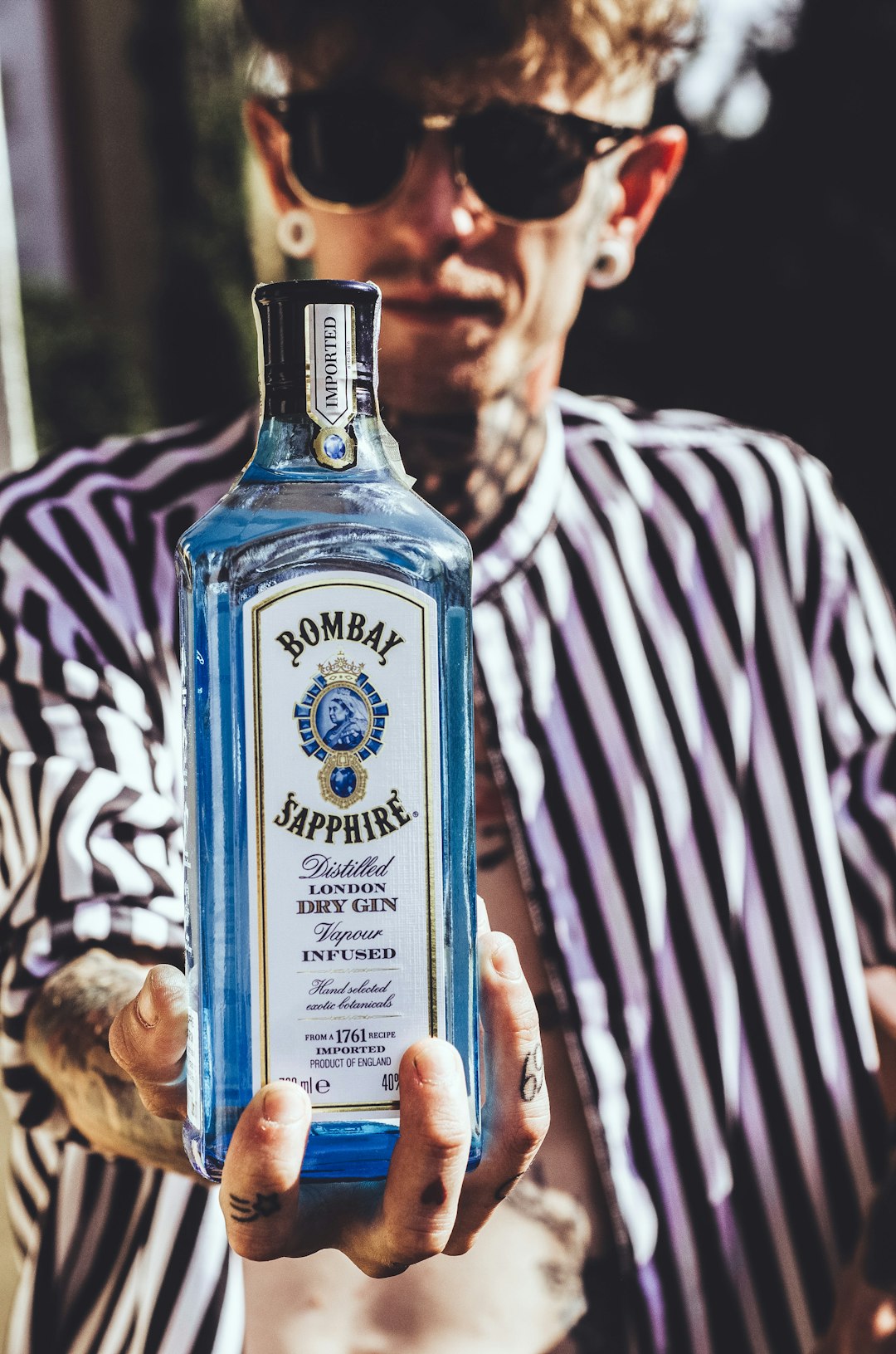 man in white and black stripe shirt holding blue glass bottle