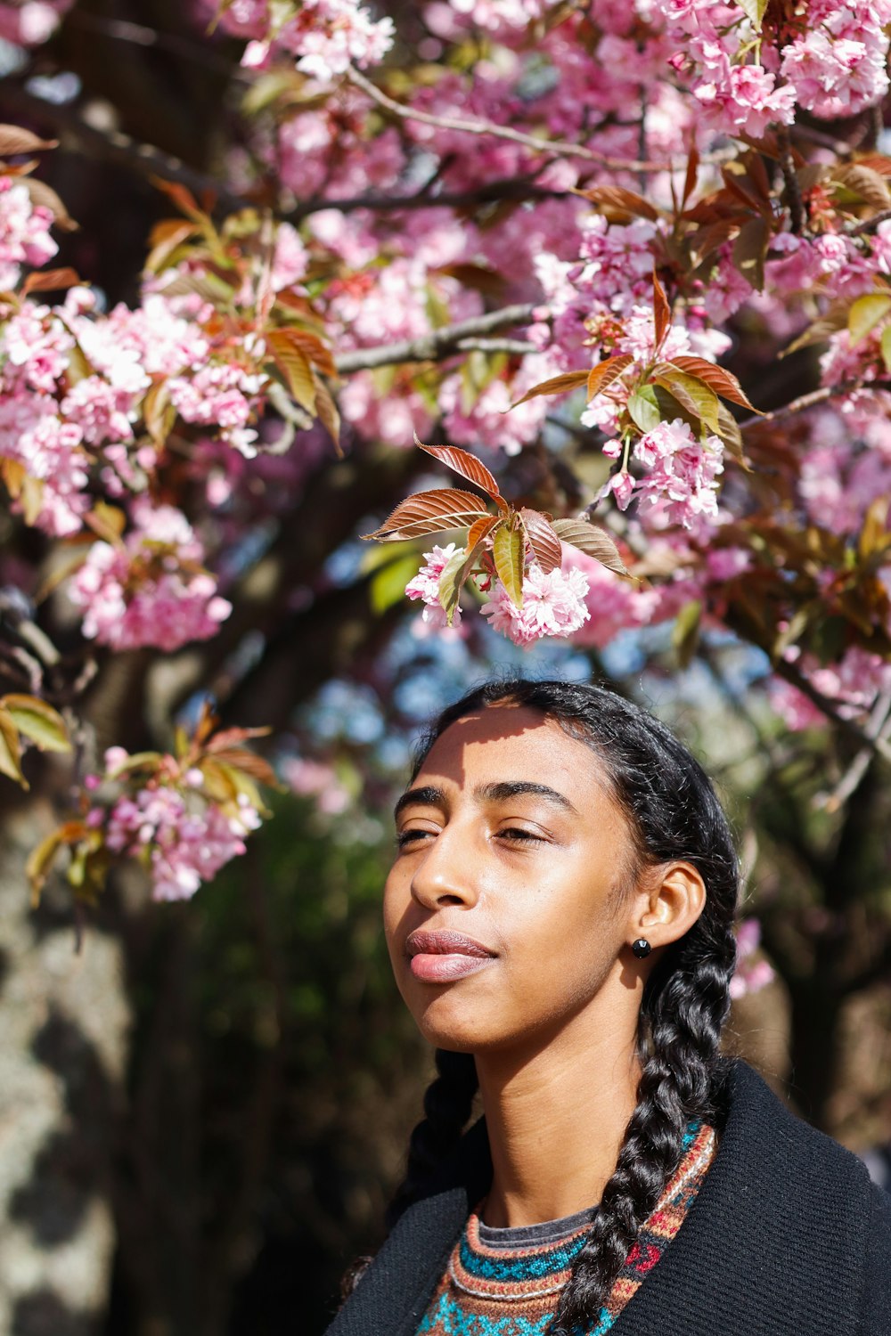 woman in black and white floral shirt standing under pink flowers