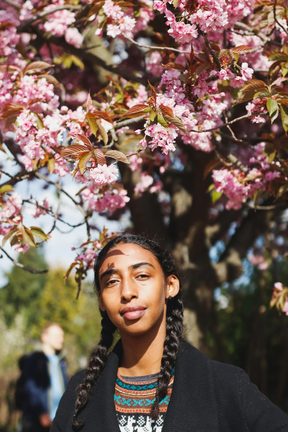 woman in black and white floral shirt standing under pink flowers