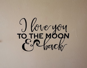 A wall decal with the phrase 'I love you to the moon & back' written in an elegant black script and bold font on a beige background.
