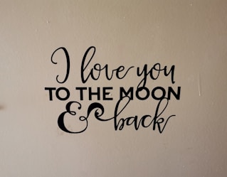 A wall decal with the phrase 'I love you to the moon & back' written in an elegant black script and bold font on a beige background.