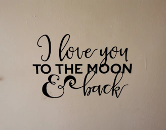 A wall decal with the phrase 'I love you to the moon & back' written in an elegant black script and bold font on a beige background.