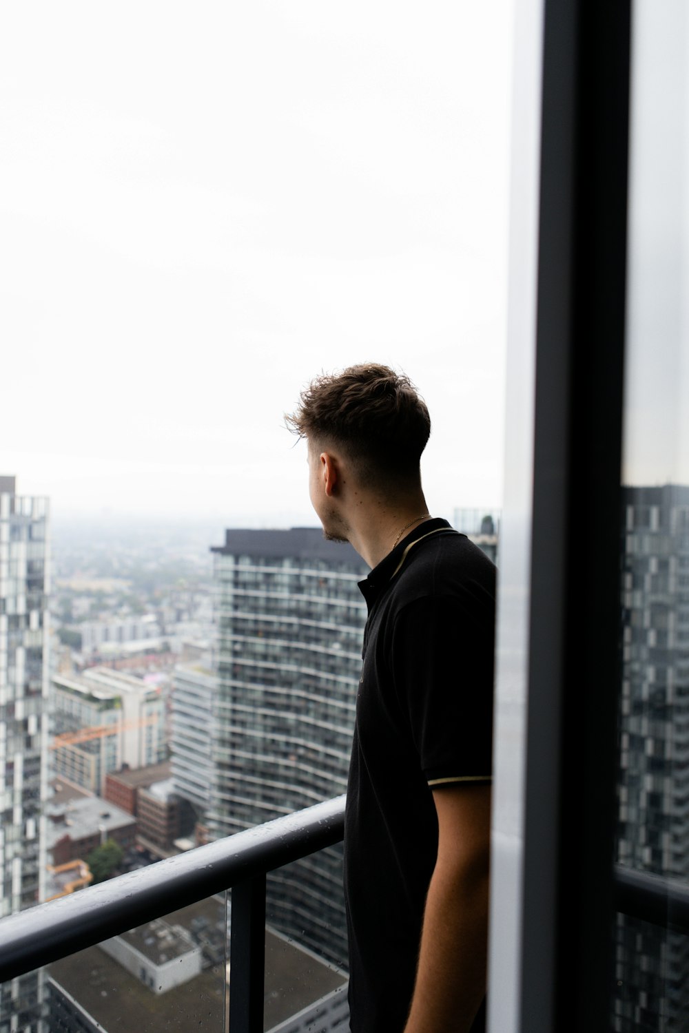 man in black crew neck t-shirt looking at the city buildings during daytime