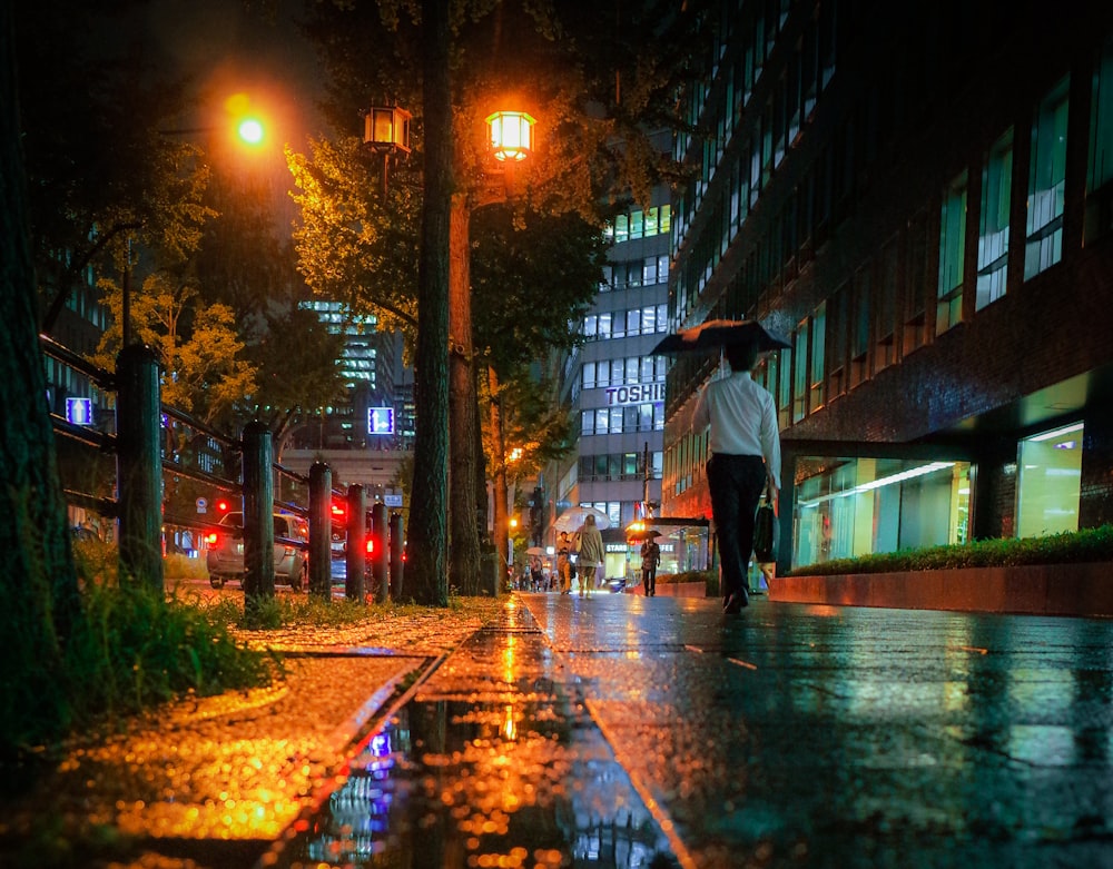 man in black jacket walking on sidewalk during night time