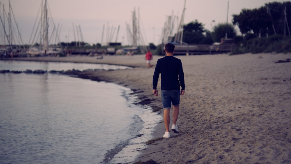 man in black long sleeve shirt and blue denim shorts standing on gray sand during daytime