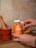 A person is holding a jar of orange flavored gummies labeled Turmeric & Ginger. The background includes a tiled wall and a wooden mortar and pestle set, creating a rustic kitchen ambiance. The jar is partially transparent, showing the gummies inside, and there is an additional bowl filled with gummies nearby.