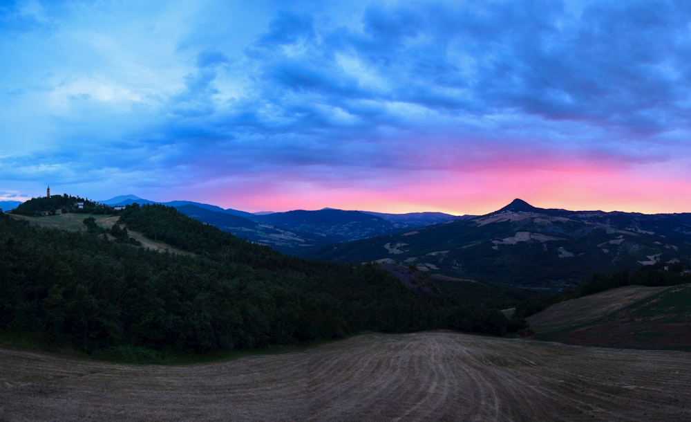 campo de hierba verde cerca de la montaña bajo el cielo azul durante el día