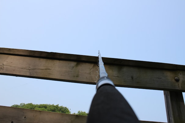 Close-up of a sturdy boat fishing rod resting against a boat railing under a clear blue sky.
