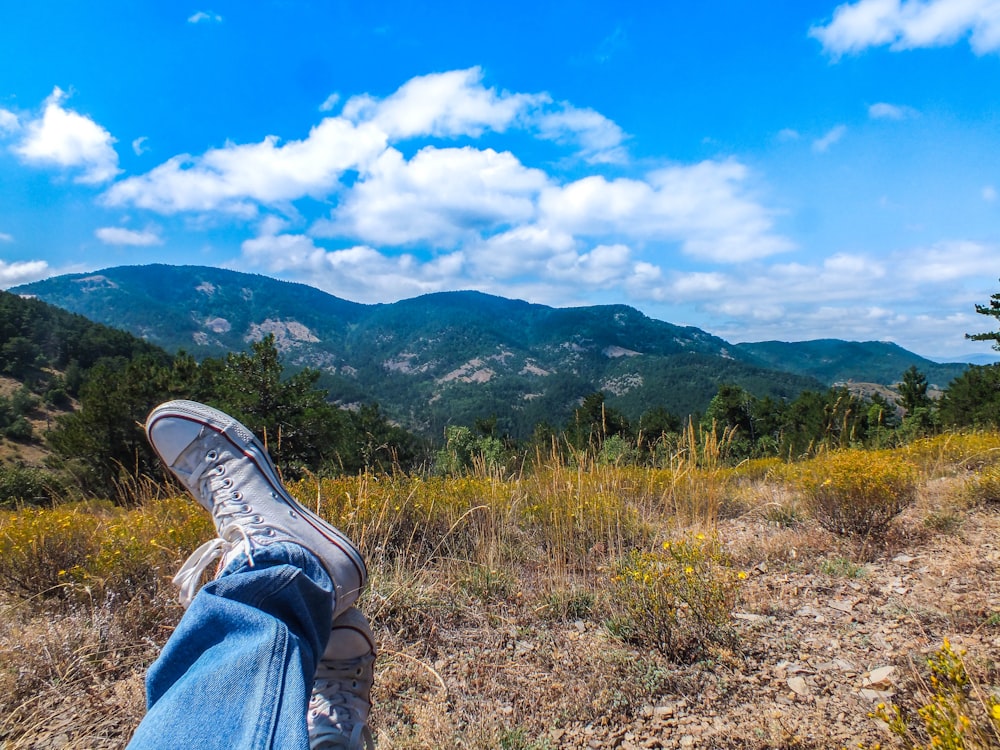 person in blue denim jeans and black and white sneakers sitting on brown grass field during