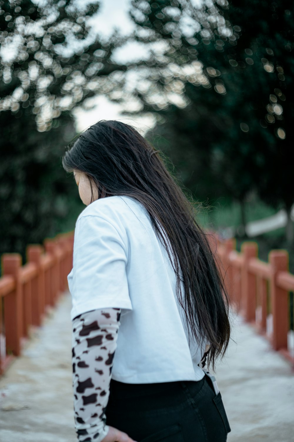 woman in white long sleeve shirt standing on red bridge during daytime