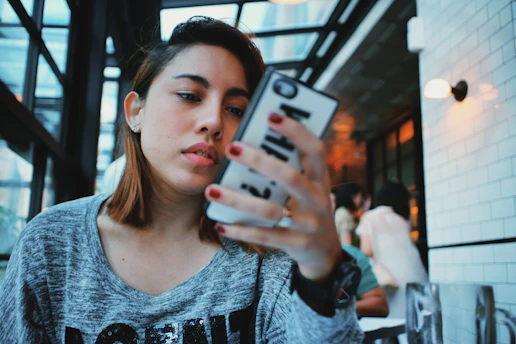 A stylish woman scrolling through a sleek handbag collection on her smartphone in a cozy cafe.