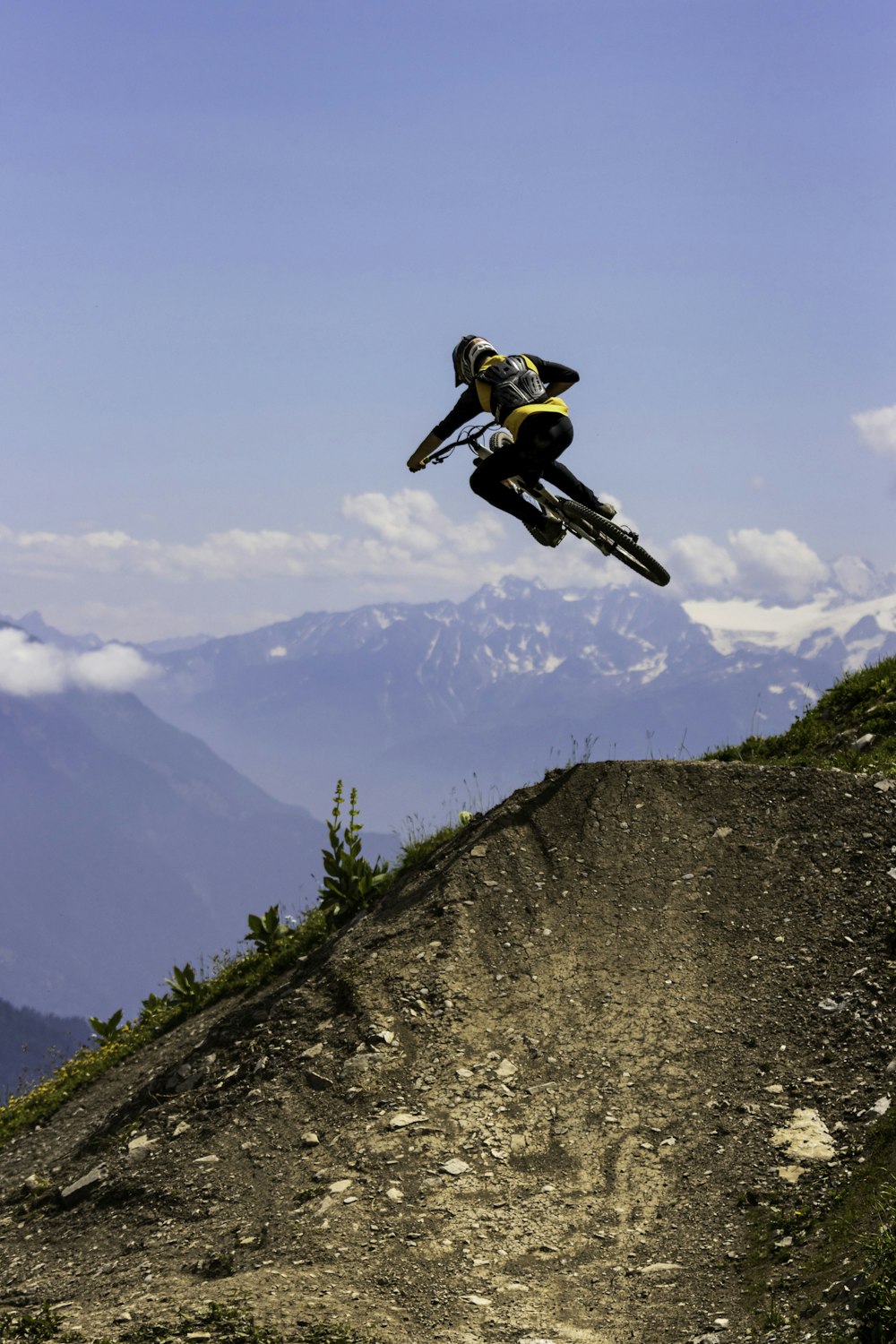 man in yellow jacket and black pants jumping on mountain during daytime