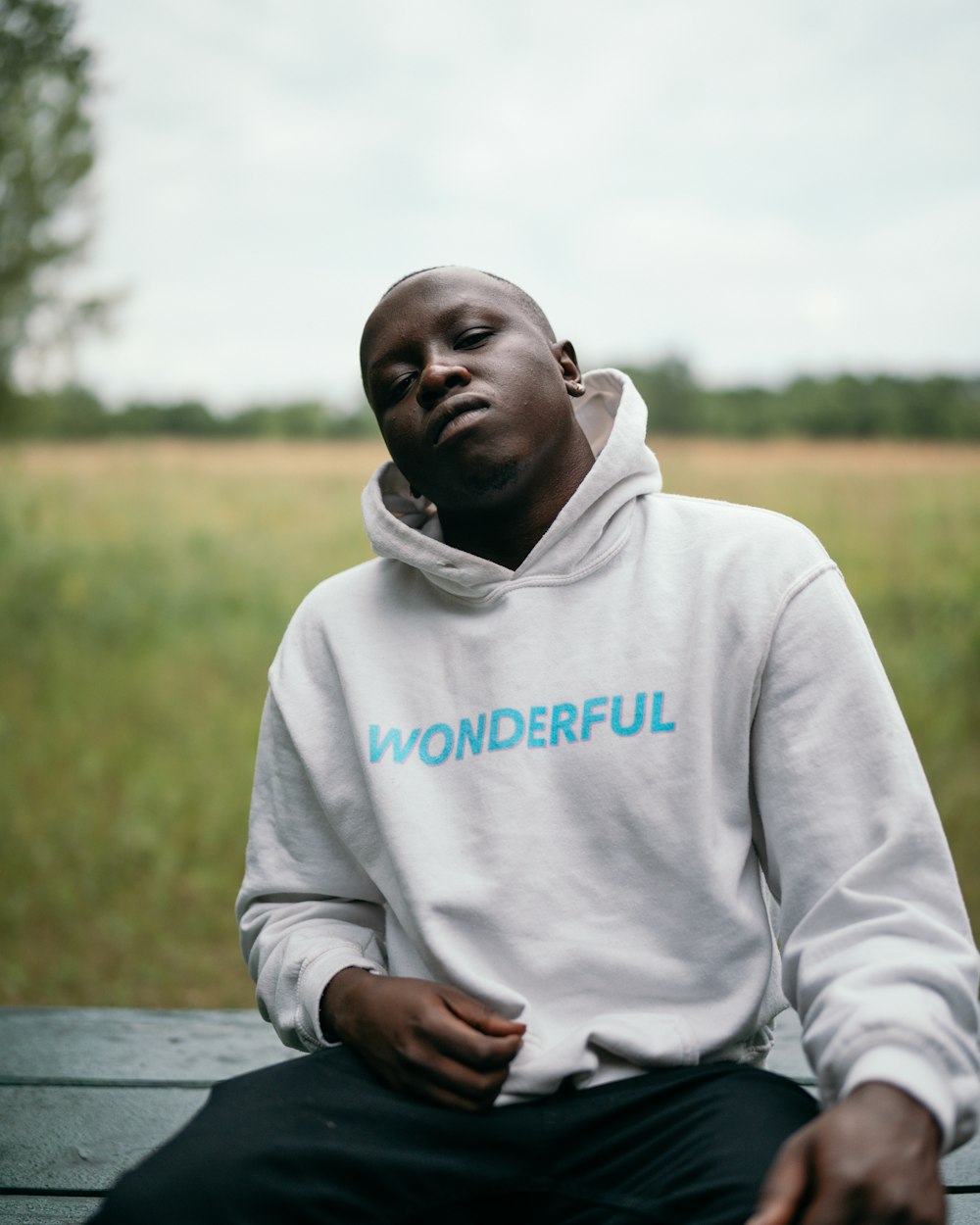 man in white pullover hoodie sitting on brown wooden bench during daytime