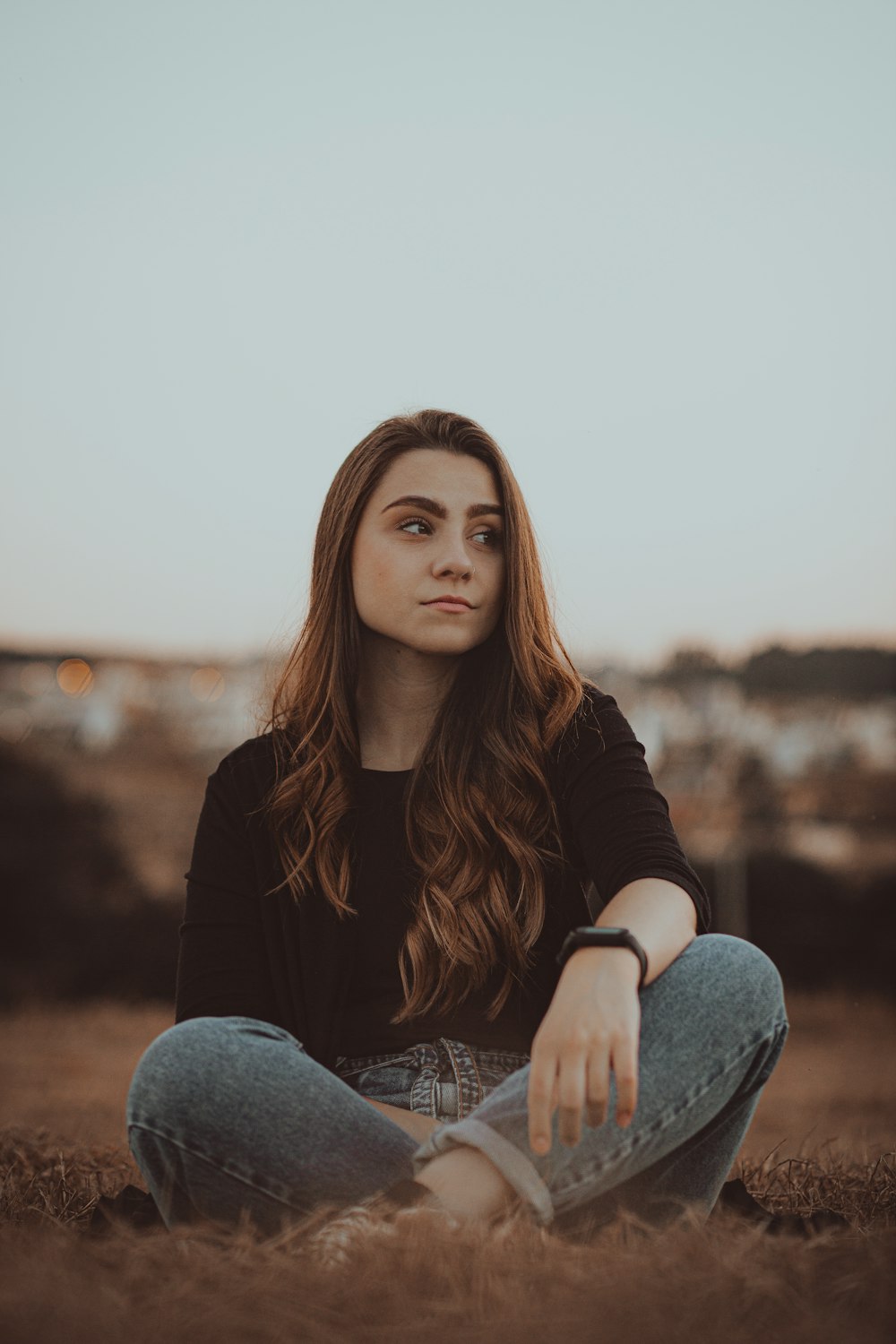 woman in black long sleeve shirt and blue denim jeans sitting on brown rock during daytime