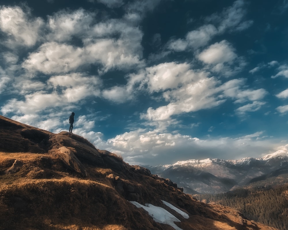 person standing on brown rock formation under white clouds and blue sky during daytime