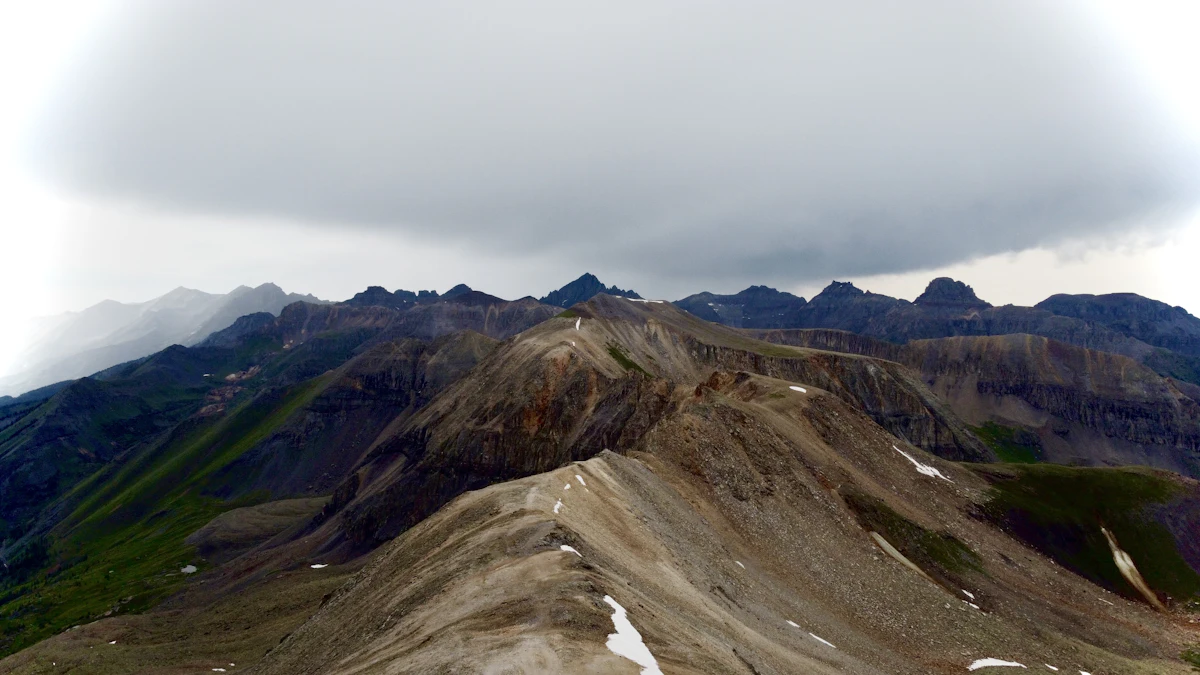 A bare ridge with snow patches near Engineer Pass above Lake City, jagged peaks behind under a storm cloud