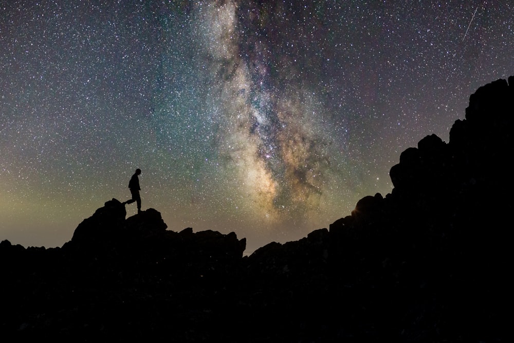 silhouette of man standing on rock under starry night