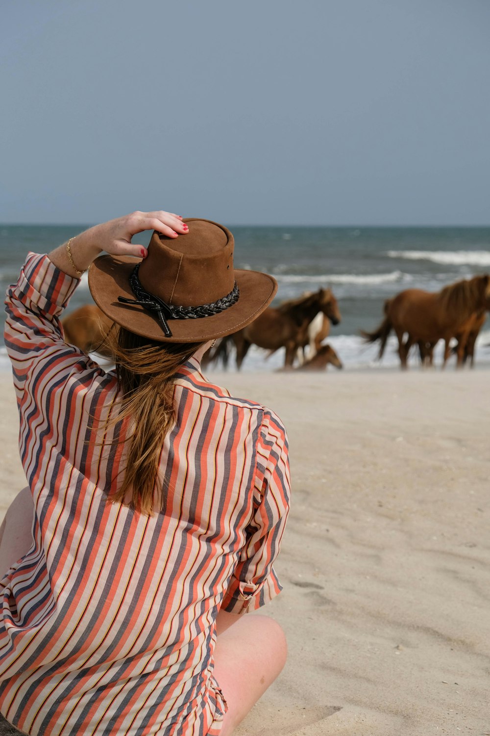 昼間のビーチに立つ茶色のカウボーイハットをかぶった女性