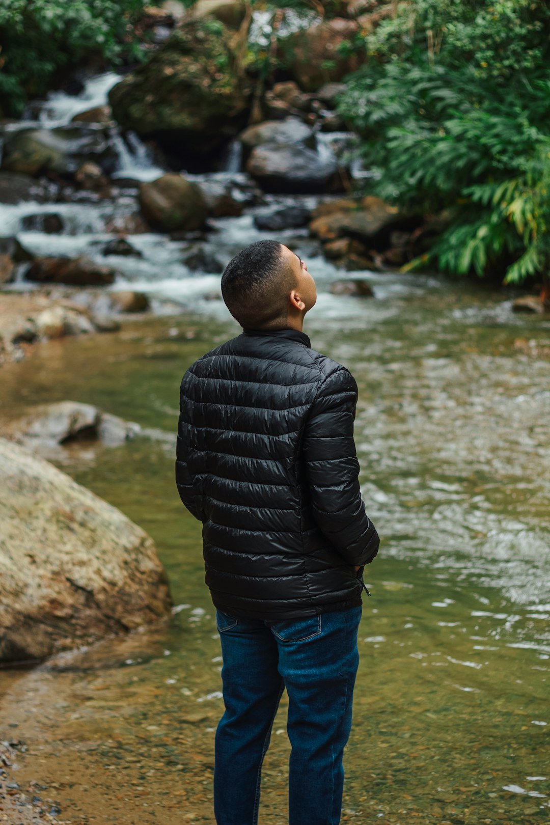 boy in black bubble jacket standing on rock near body of water during daytime