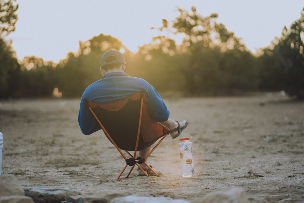 man in blue shirt sitting on brown wooden chair on beach during daytime