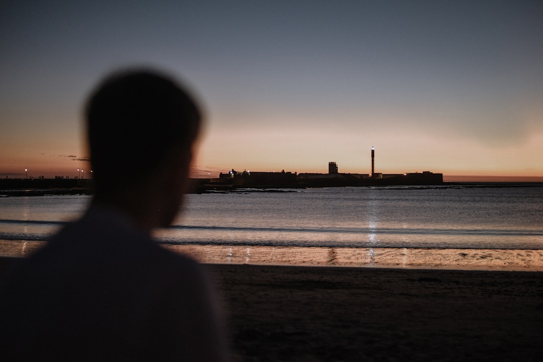 man in black hoodie standing on seashore during sunset
