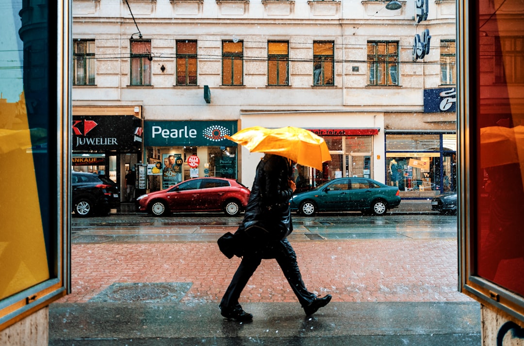 person in black jacket and black pants holding yellow umbrella walking on sidewalk during daytime