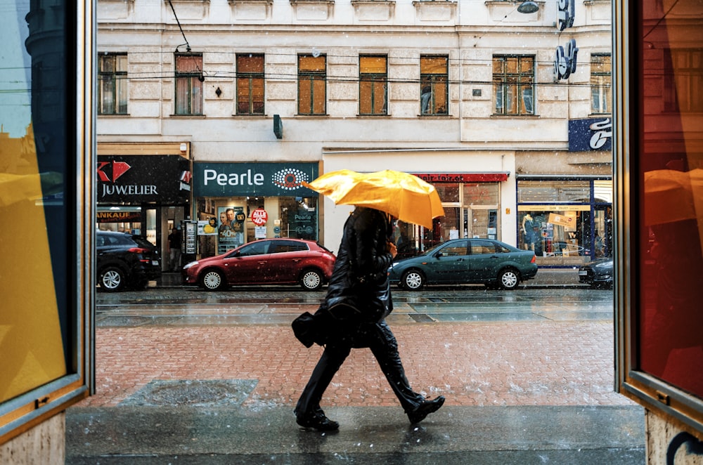 person in black jacket and black pants holding yellow umbrella walking on sidewalk during daytime