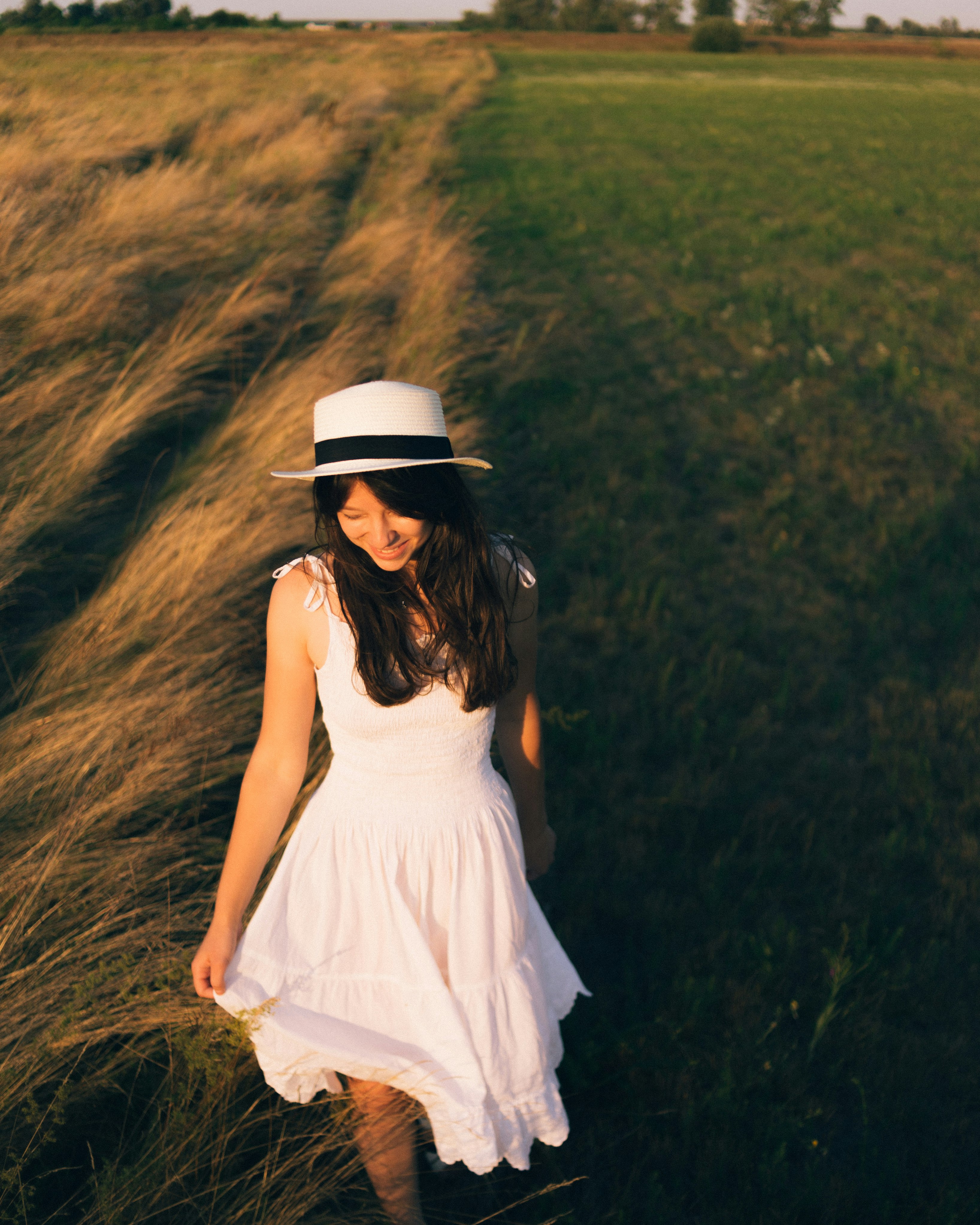 woman in white sleeveless dress wearing white hat standing on green grass field during daytime