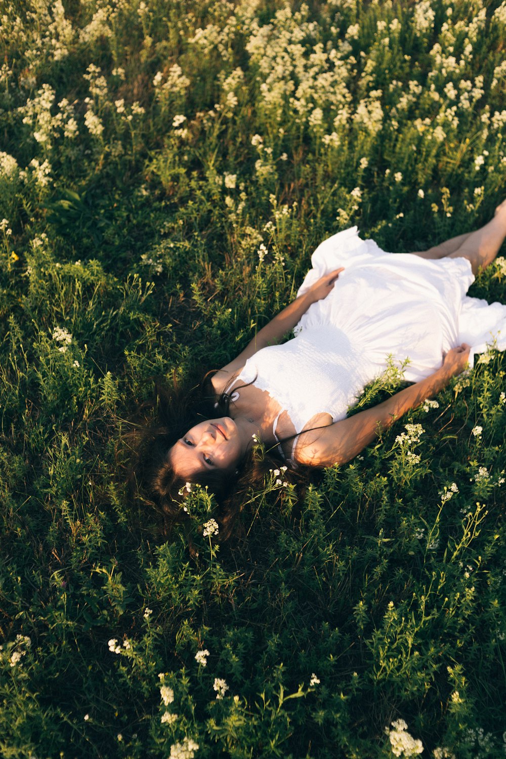 femme en robe blanche couchée sur le champ d’herbe verte pendant la journée