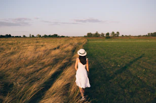 woman in white shirt and white skirt standing on green grass field during daytime