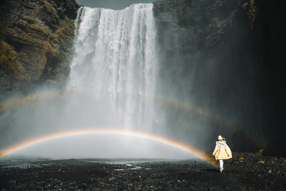 Persona en chaqueta amarilla de pie frente a cascadas durante el día