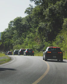 A convoy of imported cars driving through scenic Guatemalan roads at sunset.