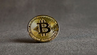 Close-up of a golden Bitcoin coin resting on a sleek black surface with subtle reflections.