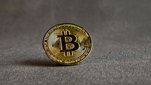Close-up of a golden Bitcoin coin resting on a dark reflective surface.