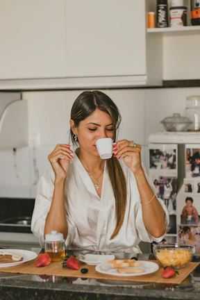 A cheerful woman enjoying a slow morning with a cup of tea, dressed in soft, flowing clothes