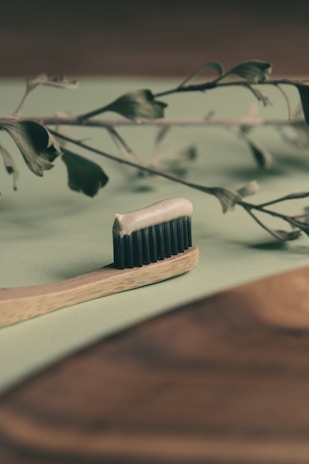 A bamboo hairbrush with natural bristles placed beside green leaves on a rustic wooden table.