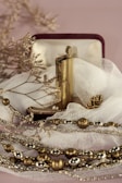 An ornate lighter rests in an open velvet-lined box, surrounded by delicate fabric. The lighter is accompanied by gold and silver-toned decorative beads and dry twigs, creating a serene and vintage aesthetic.