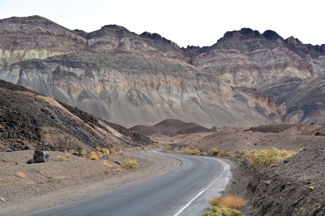 gray asphalt road near brown rocky mountain during daytime