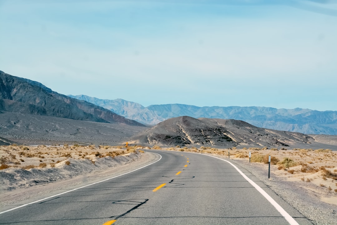 gray concrete road near brown mountain under blue sky during daytime