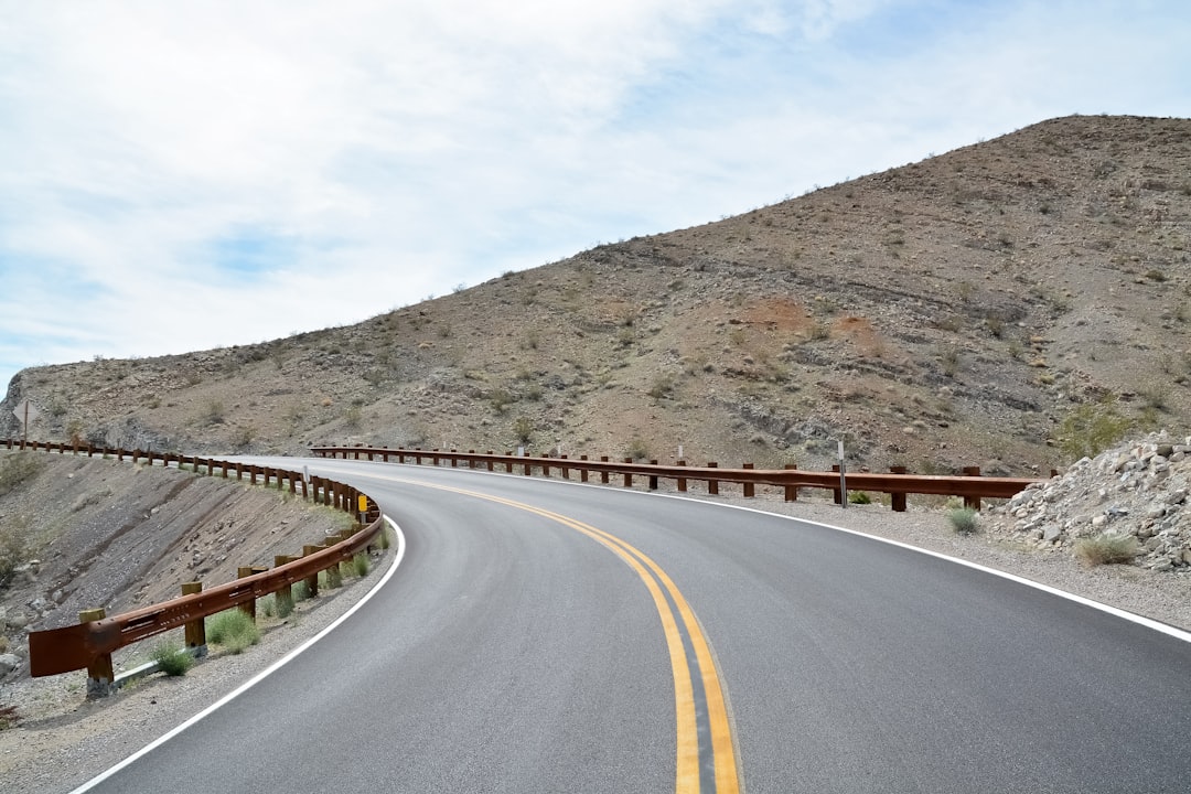 gray concrete road near brown mountain under blue sky during daytime