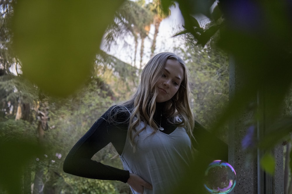 woman in white long sleeve shirt and black pants standing near green tree during daytime