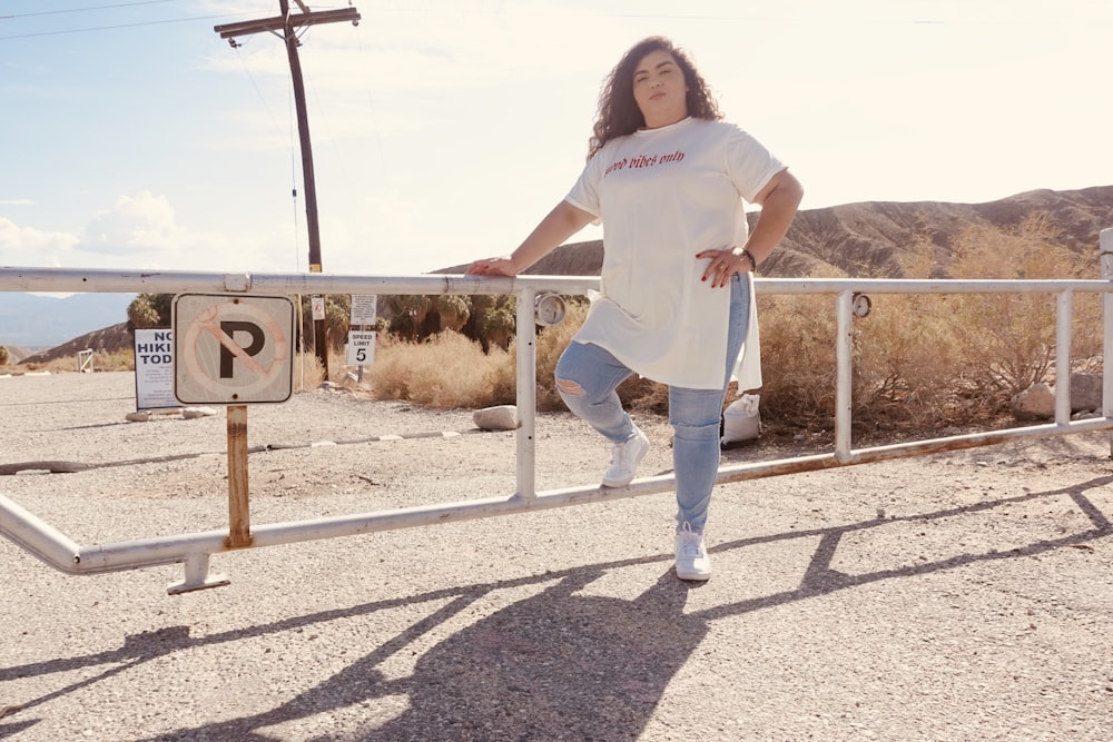 Femme en t-shirt blanc et jean bleu debout sur le trottoir en béton gris pendant la journée