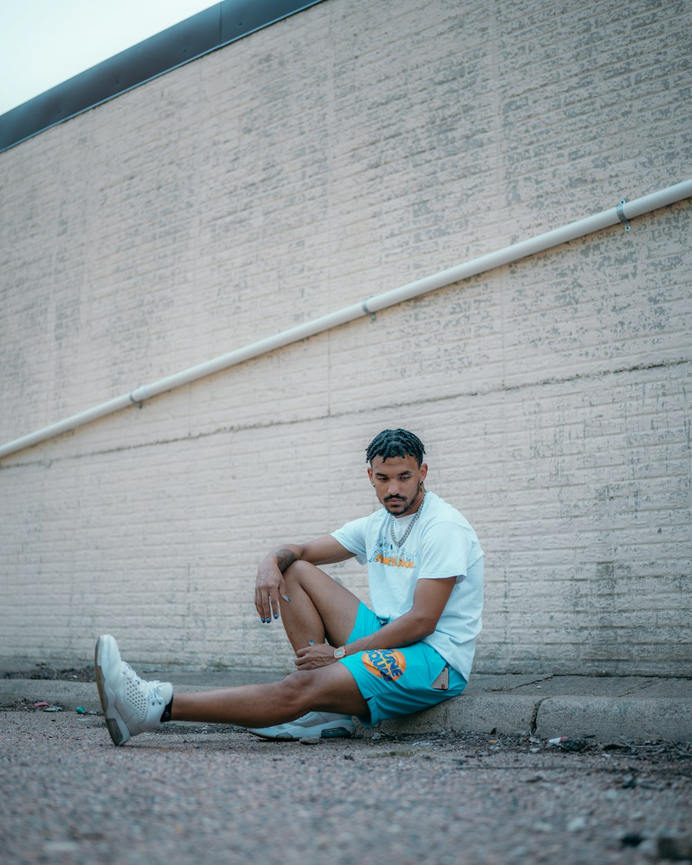 man in white crew neck t-shirt and blue denim shorts sitting on concrete wall during