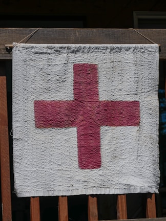 A textured fabric hanging on a wooden railing, featuring a red cross on a white background.