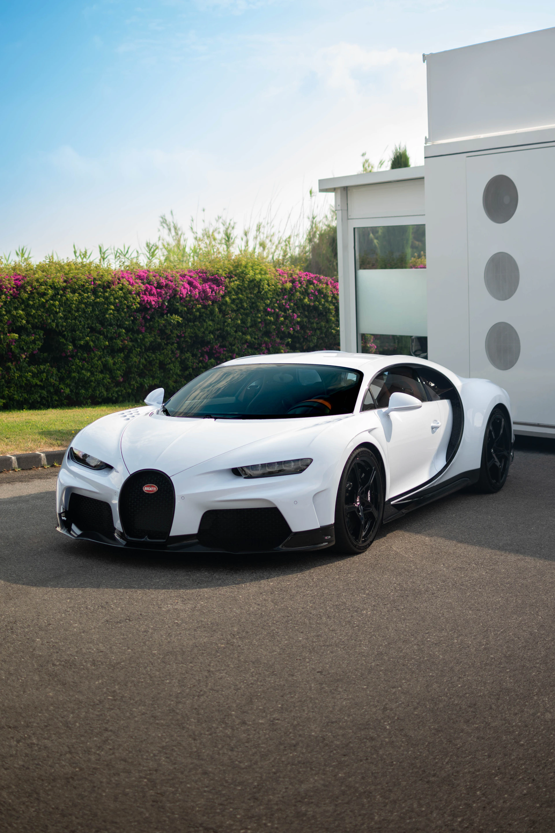 A white Bugatti Chiron sports car parked on asphalt beside a modern building